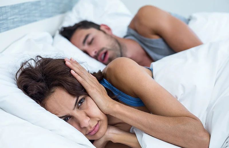 Schnarchender Mann neben seiner genervten Frau im Bett